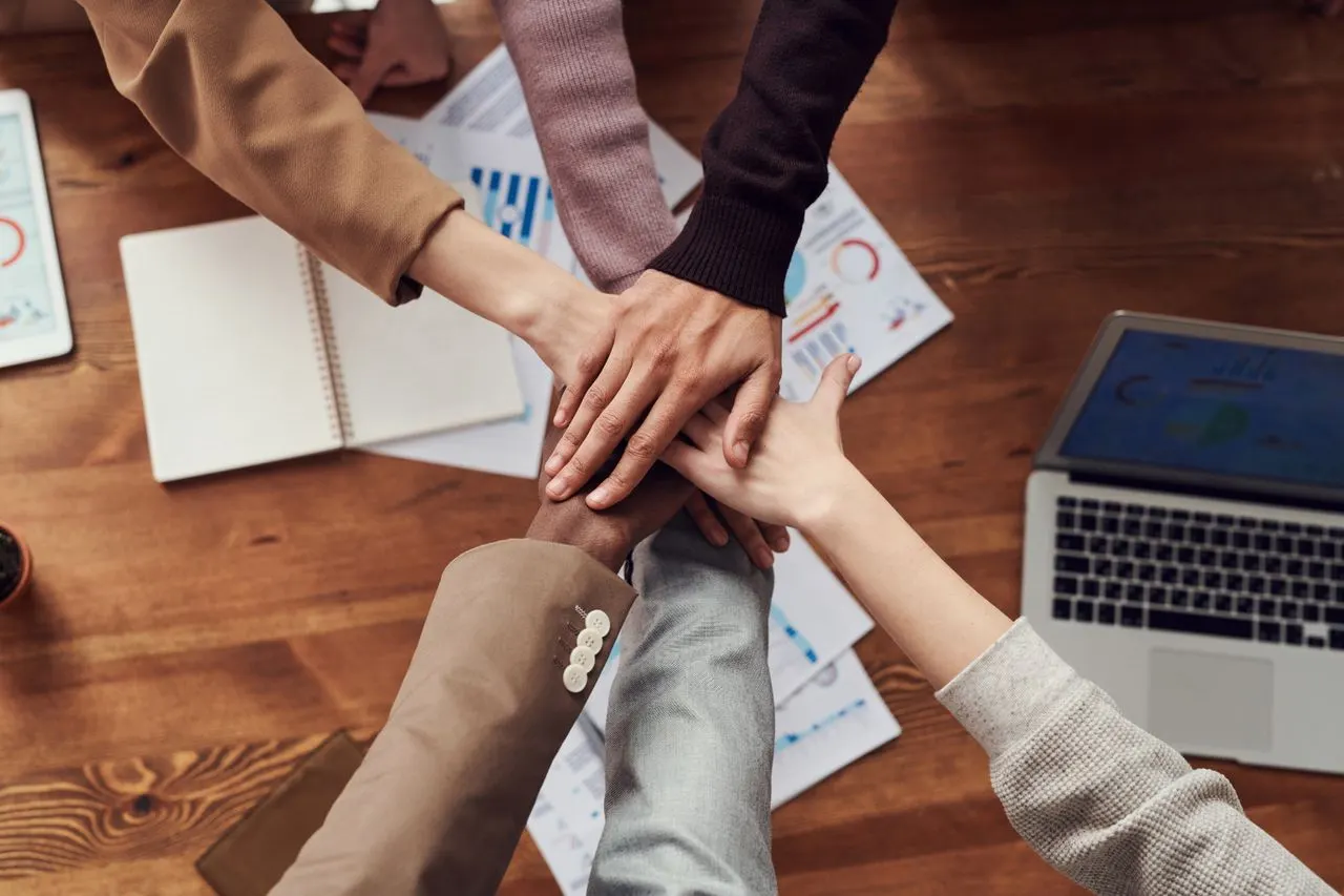 Diverse business team joining hands over financial reports at a conference table, partnership and collaboration