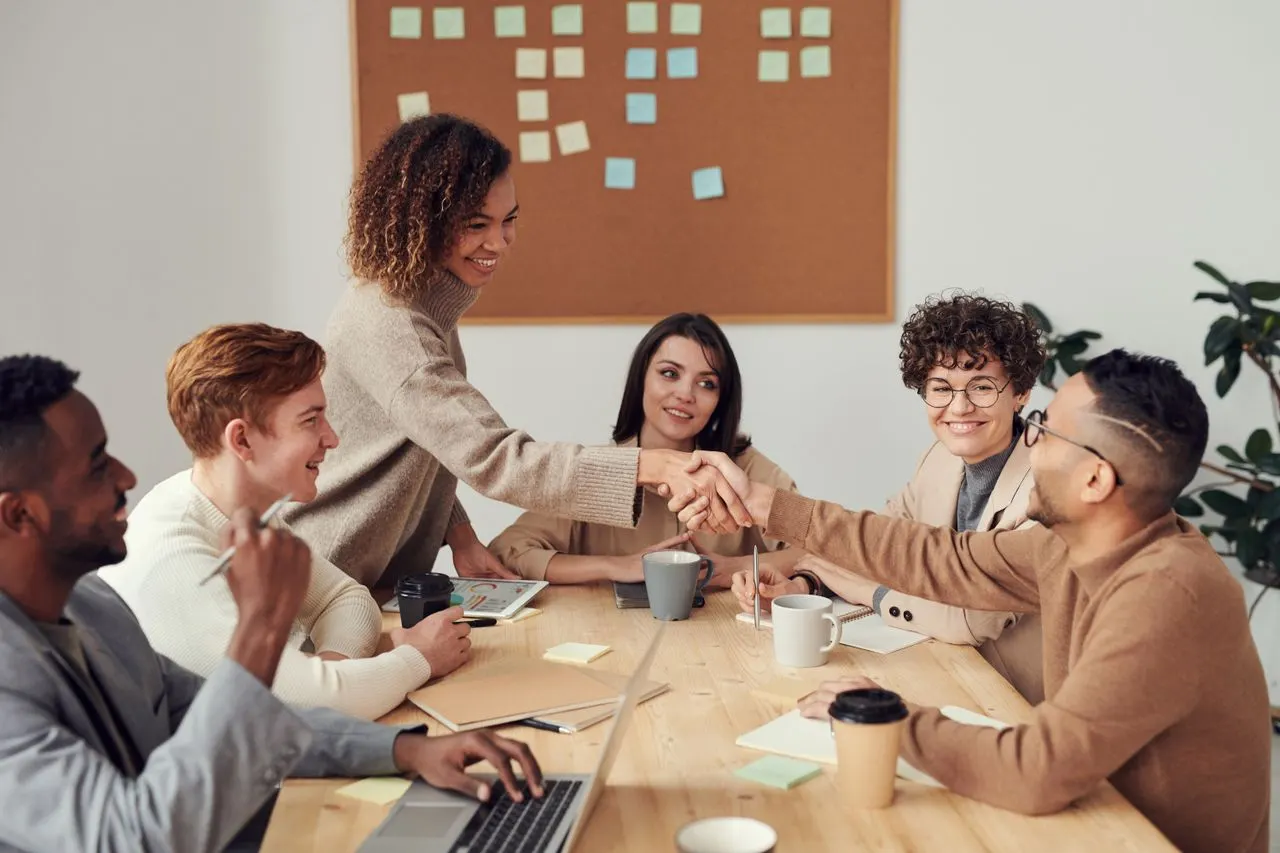 Diverse business team around a conference table exchanging a handshake, professional meeting setting